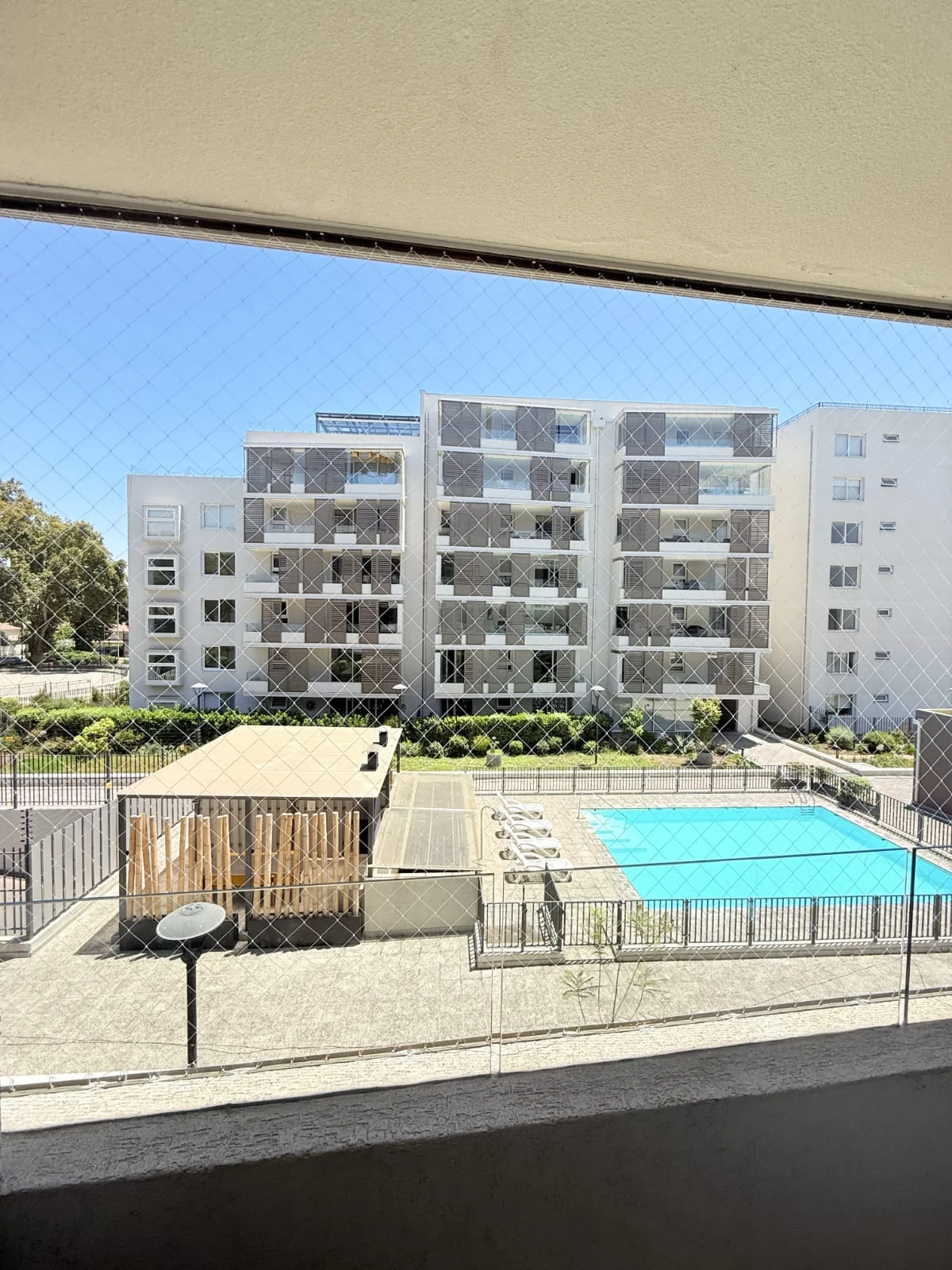 Vista de piscina y edificios a través de una malla de protección